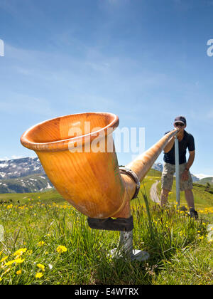 Niedrigen Winkel Sicht eines Mannes spielen ein Alphorn in den Schweizer Alpen Stockfoto