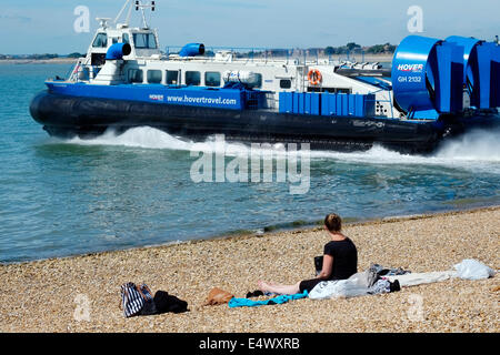 eine Frau sitzt am Strand Sonnenbaden und Uhren das Luftkissenboot fahren für die Isle Of Wight an einem heißen sonnigen Tag in Southsea uk Stockfoto