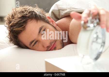 Mann im Bett Alarm ausschalten Stockfoto