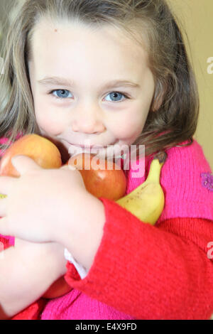 kleines Mädchen, die Früchte in ihren Armen halten Stockfoto