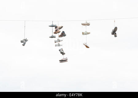 Viele alte abgenutzte Stiefel oder Schuhe, die an ein elektrisches Kabel hängen Stockfoto