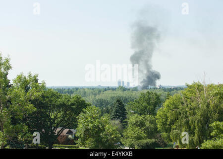 Ein Garagenfeuer, der von der anderen Seite des Urwaldes aus gesehen wird, schickt eine dicke Rauchwolke über der Skyline der Stadt in die Luft, bevor die Notfallteams eintreffen. Stockfoto