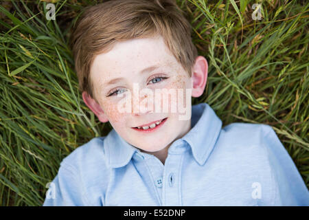 Ein Junge in ein blaues Hemd, auf dem Rücken auf dem Rasen liegend.