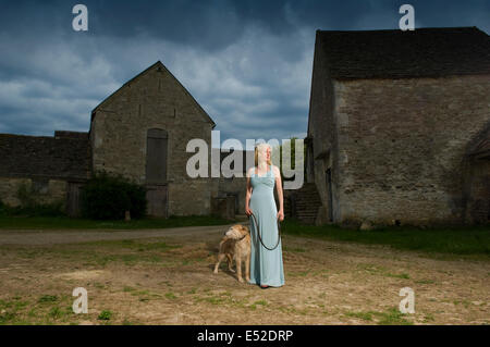 Eine Frau mit einem Lurcher Hund auf einem Hof unter Gewitterhimmel. Stockfoto