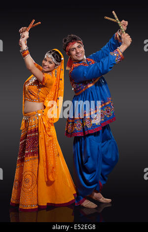 In voller Länge Portrait von jungen indischen Brautpaar durchführen Dandiya Raas auf schwarzem Hintergrund Stockfoto