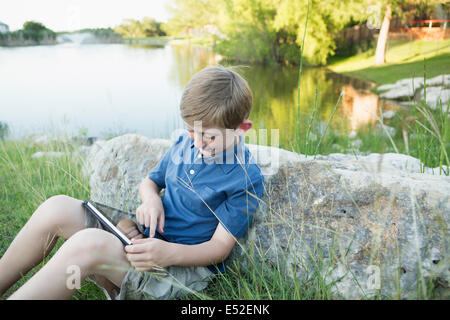 Ein kleiner Junge im Freien mit einem digitalen Tablet. Wasser zu sitzen. Stockfoto