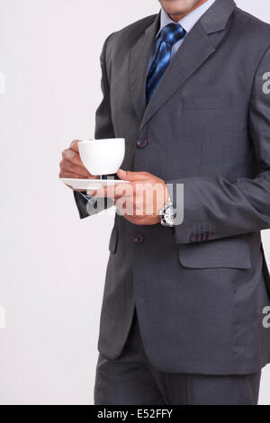 Mittelteil der Geschäftsmann hält Kaffeetasse vor grauem Hintergrund Stockfoto