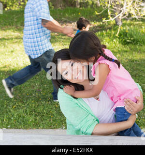 Eine Mutter im Park mit ihrer Tochter, lachen und küssen einander. Vater und Sohn auf dem Rasen laufen. Stockfoto