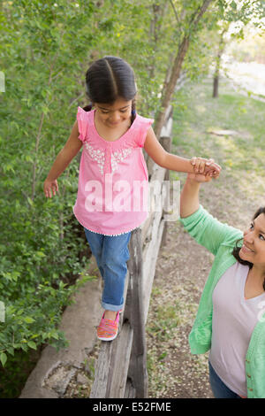 Ein junges Mädchen in einem rosa t-Shirt und Jeans, zu Fuß entlang dem Zaun an der Mutter Hand. Stockfoto