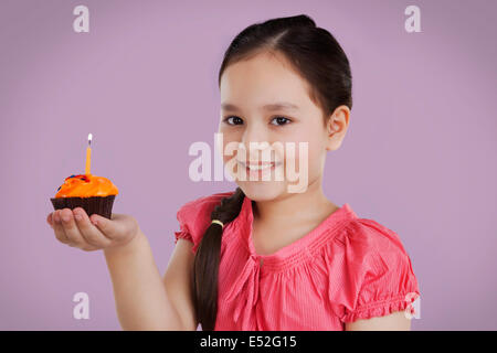 Porträt eines Mädchens hält einen kleinen Kuchen mit einer Kerze Stockfoto