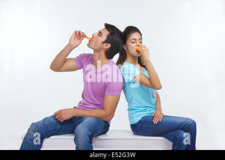 Junges Paar essen Eis am Stiehl sitzend auf Bank auf weißem Hintergrund Stockfoto