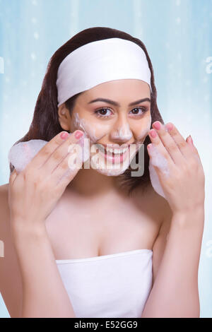 Portrait der schönen Frau schrubben Gesicht mit Seife vor blauem Hintergrund Stockfoto