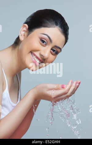 Porträt der glückliche Frau waschen Gesicht mit Wasser vor blauem Hintergrund Stockfoto