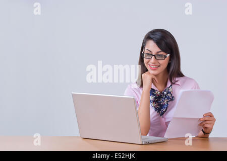 Lächelnde junge Geschäftsfrau auf Laptop am Schreibtisch im Büro arbeiten Stockfoto