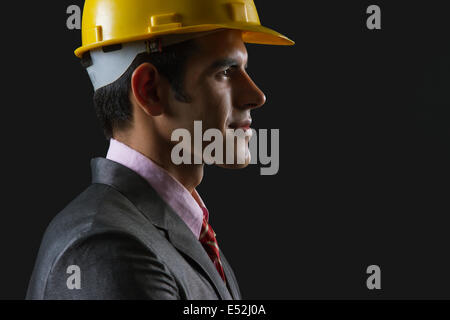 Seitenansicht des männlichen Architekten tragen Bauarbeiterhelm auf schwarzem Hintergrund Stockfoto