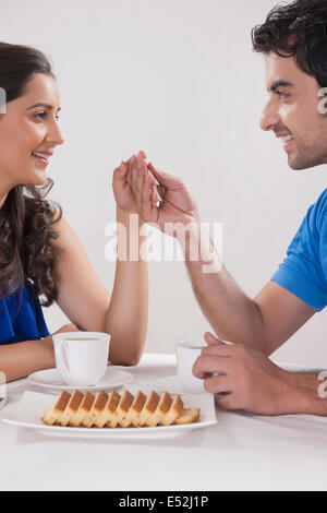 Lächelnde junge Paar Hand in Hand beim Kaffeetrinken vor weißem Hintergrund Stockfoto
