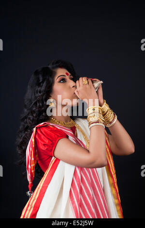 Bengali Frau bläst auf eine Muschelschale Stockfoto