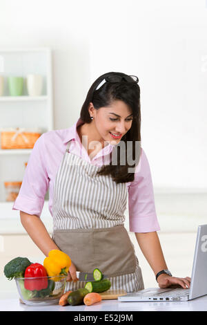 Lächelnde Geschäftsfrau Surfen am Laptop während der Zubereitung von Speisen in der Küche zu Hause Stockfoto