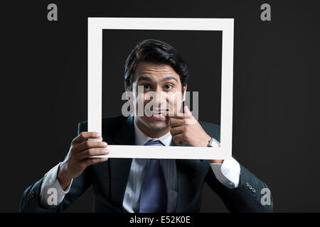 Porträt des jungen Geschäftsmann mit Finger im Mund Halterahmen auf schwarzem Hintergrund Stockfoto