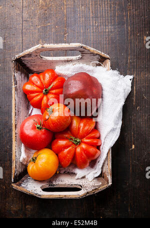 Reife frische bunte Tomaten in Holzkiste auf dunklem Holz Stockfoto