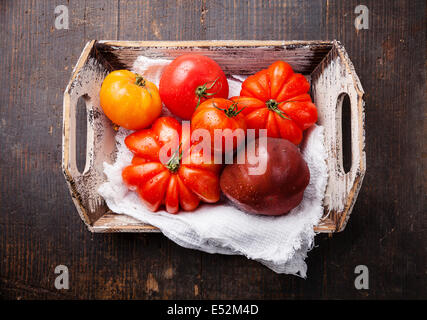 Reife frische bunte Tomaten in Holzkiste auf dunklem Holz Stockfoto