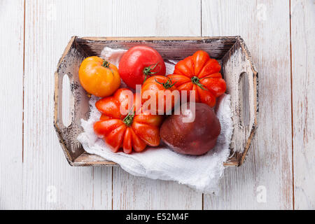 Reife frische bunte Tomaten in Holzkiste auf weißem Holz Hintergrund Stockfoto