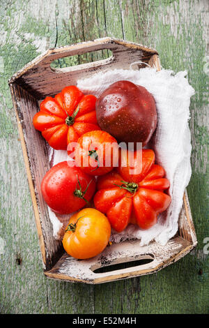 Reife frische bunte Tomaten in Holzkiste auf grünem Hintergrund aus Holz Stockfoto