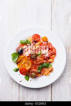 Reife frische bunte Tomaten Salat mit Olivenöl und Balsamico-Essig auf weißem Holz Hintergrund Stockfoto