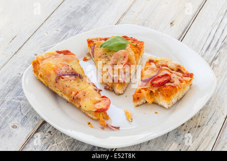 übrig gebliebene Pizza vom Vortag auf einer Platte auf einem rustikalen Holztisch Stockfoto