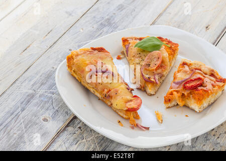 übrig gebliebene Pizza vom Vortag auf einer Platte auf einem rustikalen Holztisch Stockfoto