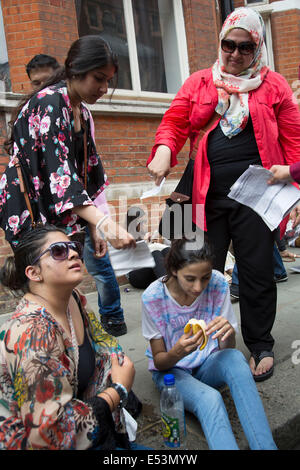 London, UK. Samstag, 19. Juli 2014. Pro-palästinensische Demonstranten in die Zehntausende marschieren durch die Londoner an die israelische Botschaft aus Protest gegen die militärische Offensive im Gazastreifen durch Israel. Mädchen, Ramadan, Fasten, ohnmächtig wird und mit Wasser und eine Banane von ihrer Familie wiederbelebt wird, wie sie Papier, um sie abkühlen winken. Bildnachweis: Michael Kemp/Alamy Live-Nachrichten Stockfoto