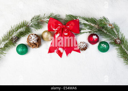 Horizontale Ansicht von Red Bow, umgeben von weißen Schnee, immergrüner Baum Zweige, Tannenzapfen und Weihnachtsschmuck Stockfoto