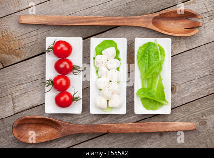 Tomaten, Mozzarella und grünem Salat Blätter auf Holztisch Hintergrund Stockfoto