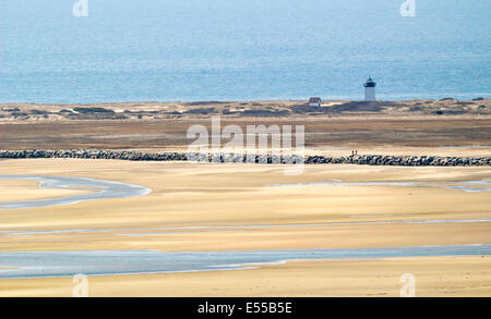 Ein Leuchtturm und ein kleines Haus am Strand mit dem Meer in Sicht und Ebbe und eine steinerne Barriere im Blick. Stockfoto