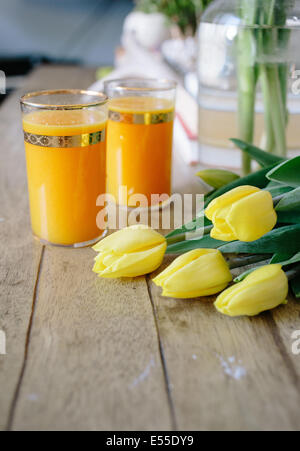 Gelbe Tulpen und neben zwei Gläser frisch gepressten Orangensaft. Stockfoto