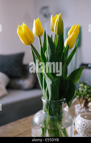 Vase mit Tulpen auf Holz Couchtisch im Wohnzimmer mit unscharfen Couch im Hintergrund. Stockfoto