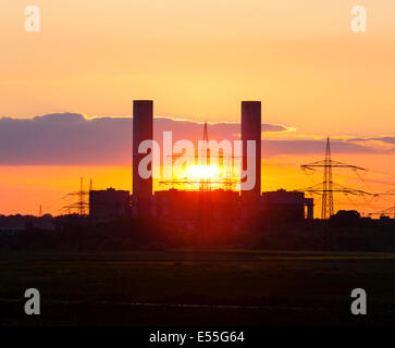 Die untergehende Sonne zwischen den Schornsteinen der ein Kohlekraftwerk. Stockfoto