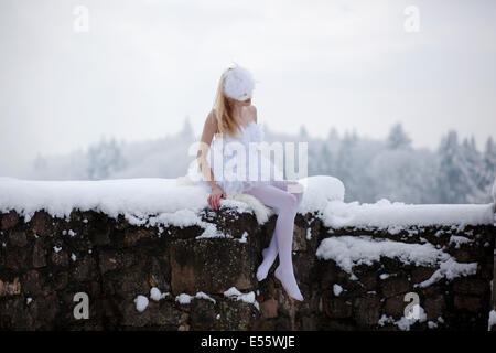 Ballerina, die auf einer Mauer im Schnee sitzend Stockfoto