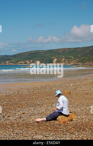 Frau sitzt auf Felsen am Strand von Vauville, Normandie, Frankreich im Juli Stockfoto