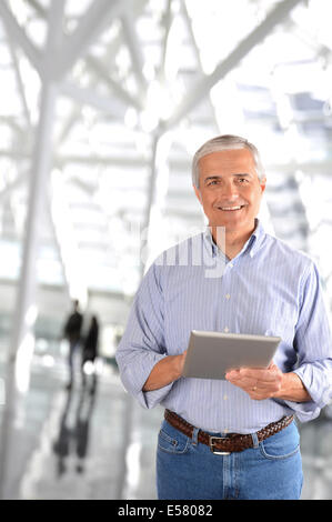 Ein reifer Geschäftsmann in der Lobby eines modernen Bürogebäudes. Die lässig gekleidete Mann lächelt und gibt verschwommene Leute Stockfoto