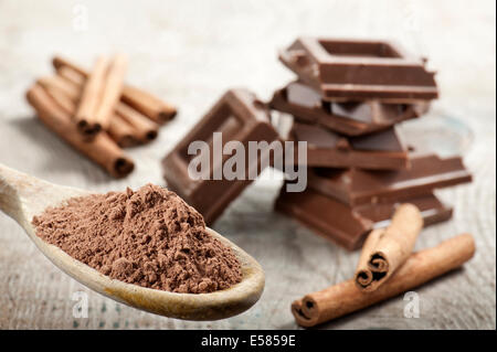 Kakaopulver auf Holzlöffel mit Zimt- und Blöcke auf Holztisch Stockfoto