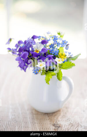 Bouquet von wilden Blumen in weißer Vase auf rustikalen Holztisch in der Nähe von Fenster, Tageslicht Stockfoto