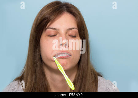 Verschlafene schöne junge Frau Zähneputzen am Morgen. Zahnbürste aus dem Mund hängen