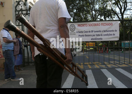 Sao Paulo, Brasilien. 23. Juli 2014. Ein Mann hält ein Paar Krücken vor der geschlossenen Tür der philanthropischen Krankenhaus Santa Casa Sao Paulo, Brasilien, am 23. Juli 2014. Klinikum Santa Casa, das größte philanthropische Krankenhaus innen Lateinisches Amerika, unterbricht die Dringlichkeit und Notfall-Service ab Dienstag Nacht aufgrund des Mangels an Geld, Medikamente und Materialien zu kaufen. © Rahel Patras/Xinhua/Alamy Live-Nachrichten Stockfoto