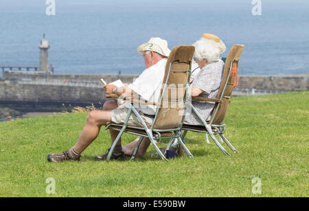 Ältere Menschen lesen und genießen das warme Wetter bei Whitby, North Yorkshire, England, UK Stockfoto