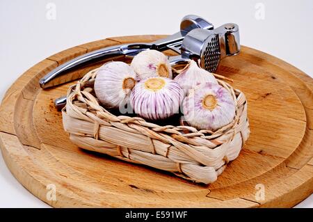 Knoblauch Zwiebeln in einem Weidenkorb mit einer Knoblauch drücken Sie auf einem Holzbrett. Stockfoto