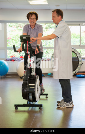 Physiotherapeut hilft einen Patienten einen Heimtrainer zu fahren Stockfoto