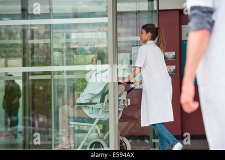 Ärztin, schob ein Patient sitzt auf einem Stuhl Stockfoto