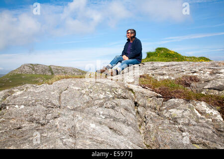 Applying weibliche Wanderer sitzen hoch auf Felsvorsprung in Barra, äußeren Hebriden, Schottland Stockfoto