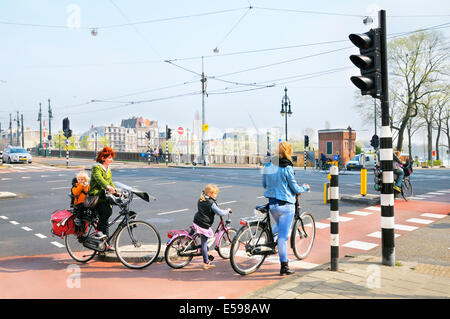 Frauen und Kinder auf Fahrrädern warten an einer Straßenkreuzung, Amsterdam, Niederlande Stockfoto